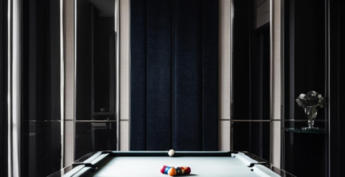 A modern billiards room with dark walls, a sleek pool table, and sophisticated lighting.