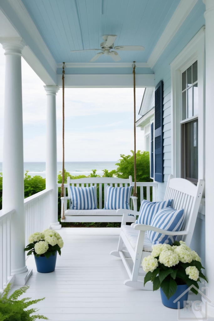 A serene coastal porch with white painted wood, a light blue ceiling, a white porch swing, a white rocking chair, blue and white striped pillows, and potted white hydrangeas, overlooking the ocean.