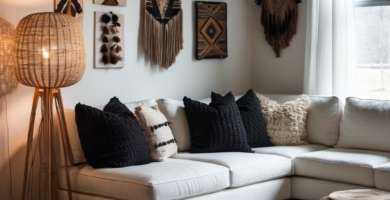 A cozy living room featuring a white L-shaped sectional sofa adorned with black and cream textured pillows, a large shaggy rug, and a woven rattan floor lamp. The walls are decorated with various tribal-inspired textile wall hangings, and a dark polished floor adds depth to the space.