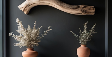 A dark charcoal-painted foyer features a light grey concrete console table adorned with two terracotta vases holding dried botanicals. Above the table, a large, curved piece of light-colored driftwood serves as a striking wall art piece, complementing the rustic ceiling beams.