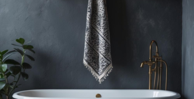 A moody dark bohemian bathroom featuring a black clawfoot bathtub against a textured charcoal wall. Brass fixtures, a patterned rug, and glowing candles create a warm, inviting atmosphere.