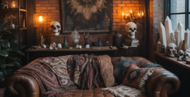 A dark boho loft living room featuring an exposed brick wall, a brown leather Chesterfield sofa, and an eclectic mix of decor. Industrial pendant lights illuminate a vintage area rug and a console table adorned with skulls and crystals, creating a cozy and unique atmosphere.
