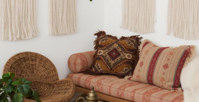 A cozy boho living room featuring a wooden daybed with terracotta cushions, a rattan chair, and a wooden coffee table on a jute rug. The white walls are adorned with macrame wall hangings, and a trailing plant adds a touch of greenery, creating a warm and inviting space.