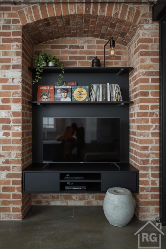 An urban industrial TV wall design integrated into an exposed brick archway. It features matte black floating shelves, a TV cabinet, a large flat-screen television, decorative records, a trailing plant, and an industrial-style wall lamp, showcasing a stylish tv wall design.