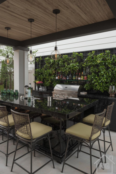A modern outdoor kitchen and bar area featuring a large black granite island, built-in grill, and several bar stools. A lush green vertical garden serves as a vibrant backdrop, complemented by wood paneling on the ceiling and contemporary pendant lighting.