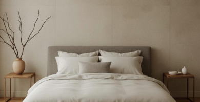 A minimalist Japandi bedroom featuring an upholstered bed with light neutral bedding, two wooden nightstands, and a textured area rug over herringbone wood flooring. The walls are a light greige paneled design, and the room is decorated with a ceramic vase holding dried branches, embodying an earthy, calm aesthetic.